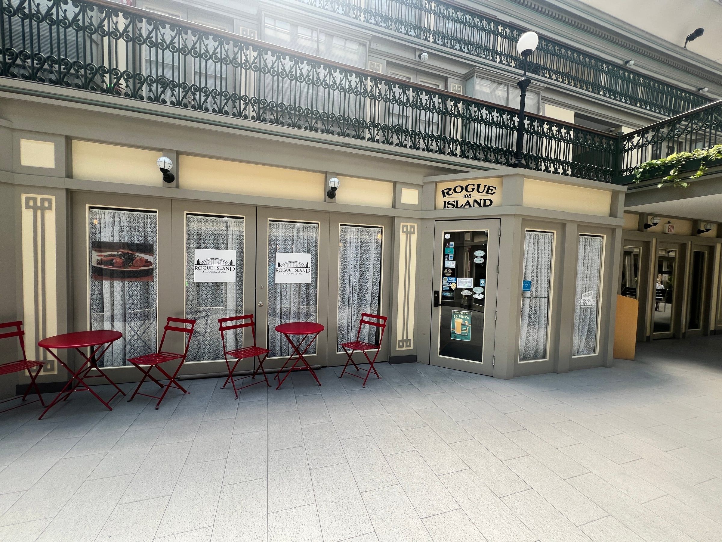 Rogue Island's storefront inside The Arcade Providence, red bistro tables out front