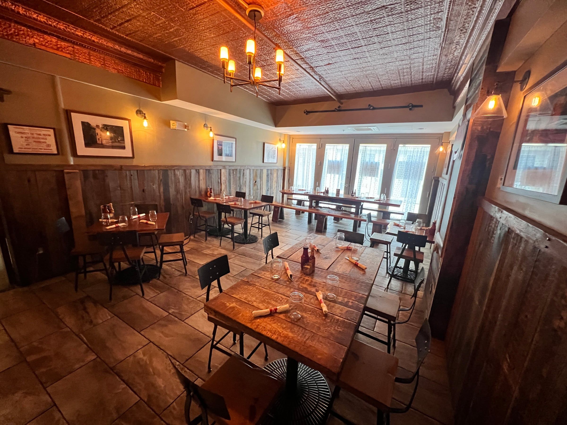 The private dining room by day — farm tables, benches, tin ceiling, and French doors onto the Arcade
