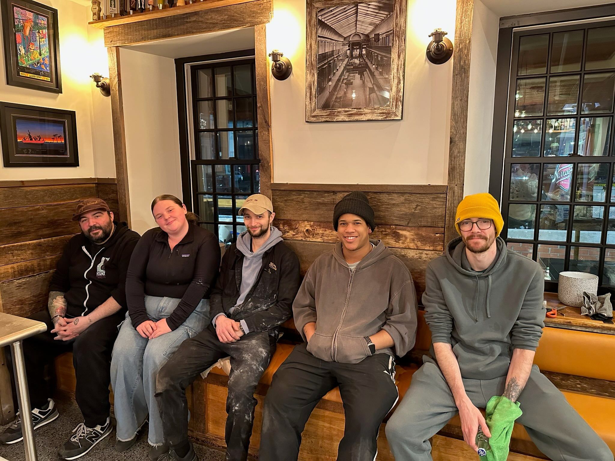Five of the Rogue Island crew smiling on the dining-room bench under the vintage Arcade print